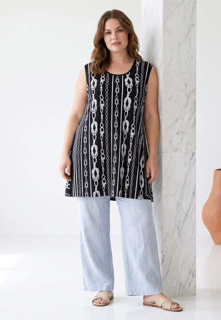 Ολόσωμη λήψη με αέρινη γυναικεία τουνίκ plus size σε μαύρο χρώμα με λευκά μοτίβα αλυσίδας, συνδυασμένη με γαλάζιο παντελόνι.