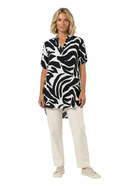 Ολόσωμη λήψη μοντέλου που φοράει ασύμμετρη ασπρόμαυρη τουνίκ σε μεγάλα μεγέθη. Ξεχωρίζει το αφηρημένο πριντ και η κομψή λαιμόκοψη V.