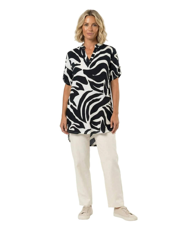 Ολόσωμη λήψη μοντέλου που φοράει ασύμμετρη ασπρόμαυρη τουνίκ σε μεγάλα μεγέθη. Ξεχωρίζει το αφηρημένο πριντ και η κομψή λαιμόκοψη V.