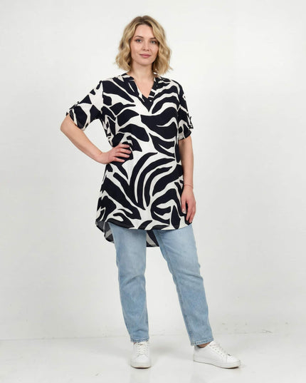 Γυναικεία ασύμμετρη ασπρόμαυρη καλοκαιρινή τουνίκ σε μεγάλα μεγέθη με αφηρημένο πριντ. Ολόσωμη λήψη του μοντέλου που τη συνδυάζει με τζιν.