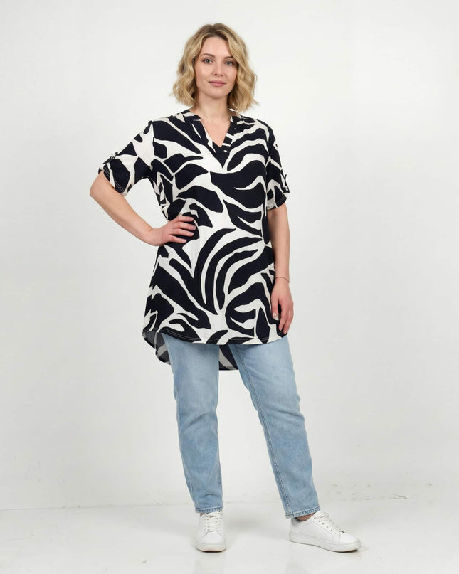 Γυναικεία ασύμμετρη ασπρόμαυρη καλοκαιρινή τουνίκ σε μεγάλα μεγέθη με αφηρημένο πριντ. Ολόσωμη λήψη του μοντέλου που τη συνδυάζει με τζιν.