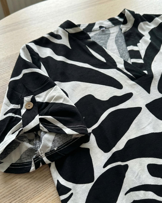 Κοντινή λεπτομέρεια της ασπρόμαυρης τουνίκ σε μεγάλα μεγέθη πάνω σε τραπέζι. Διακρίνεται το αφηρημένο print και το ρυθμιζόμενο μανίκι με κουμπί.