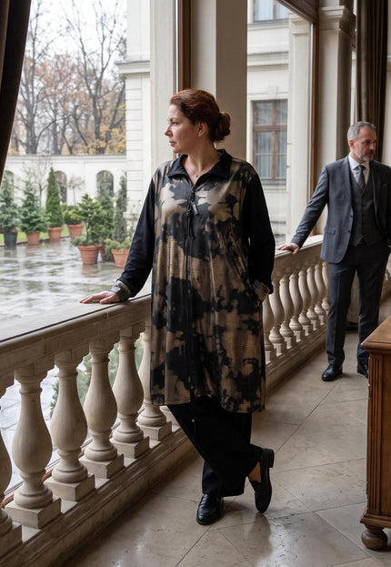 Ολόσωμη λήψη με επίσημη γυναικεία ζακέτα σε μεγάλα μεγέθη, σε μαύρο χρώμα με χρυσό-μπρονζέ μοτίβο, φορεμένη σε κομψό εσωτερικό χώρο.