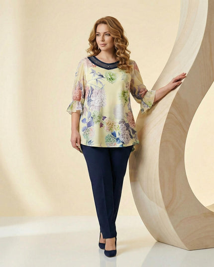 Επίσημη εβαζέ τουνίκ σε κίτρινο χρώμα με φλοράλ σχέδια και διακοσμητικές πέρλες στο ντεκολτέ. Ολόσωμη λήψη plus size ρούχου συνδυασμένου με μπλε παντελόνι.