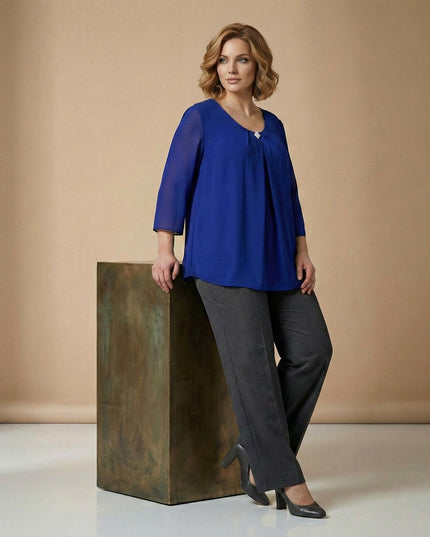 Επίσημη εβαζέ τουνίκ σιφόν σε μπλε ρουά με καρφίτσα, σε ολόσωμη λήψη. Κομψό σχέδιο με μανίκια 7/8 και αέρινη γραμμή που κολακεύει τα μεγάλα μεγέθη.