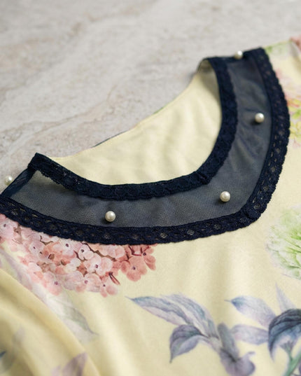 Κοντινή λεπτομέρεια λαιμόκοψης σε κίτρινη φλοράλ τουνίκ για μεγάλα μεγέθη, διακοσμημένη με μπλε τούλι, δαντέλα και πέρλες.