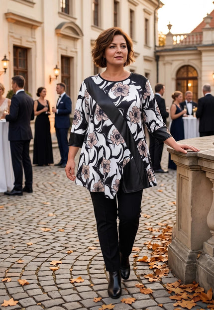 Ολόσωμη λήψη με γυναίκα που φοράει επίσημη φλοράλ τουνίκ σε μεγάλα μεγέθη, συνδυασμένη με μαύρο παντελόνι σε κομψή εκδήλωση.