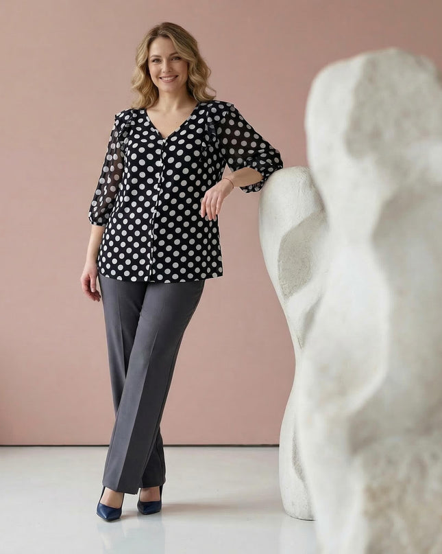 Ολόσωμη λήψη με γυναικεία σκούρα μπλε τουνίκ με λευκό πουά σε μεγάλα μεγέθη. Φορεμένη με γκρι παντελόνι, αναδεικνύει τα αέρινα 3/4 μανίκια σιφόν.