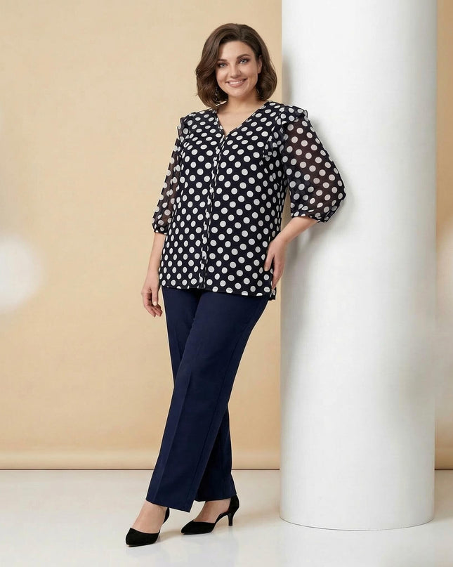 Ολόσωμη λήψη γυναικείας σκούρας μπλε τουνίκ με λευκό πουά σε μεγάλα μεγέθη με μανίκια 3/4 και V λαιμόκοψη. Φορεμένη από μοντέλο που ακουμπάει σε κολώνα.