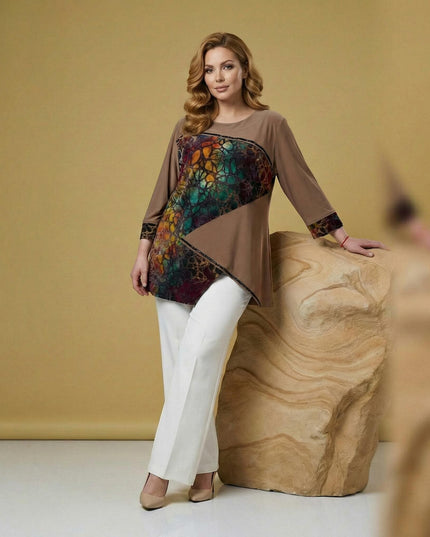 Επίσημη καφέ τουνίκ plus size με ασύμμετρη εμπριμέ φάσα και μανίκια 7/8. Ολόσωμη λήψη που δείχνει την άνετη ριχτή γραμμή συνδυασμένη με λευκό παντελόνι.