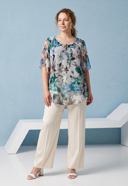 Ολόσωμη λήψη με γυναικεία επίσημη κλος τουνίκ σε μεγάλα μεγέθη, με εντυπωσιακό φλοράλ σχέδιο σε μπλε και πράσινες αποχρώσεις και λευκό παντελόνι.