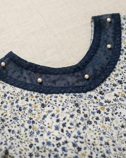 Κοντινή λεπτομέρεια λαιμόκοψης σε επίσημη λευκή φλοράλ τουνίκ για μεγάλα μεγέθη, διακοσμημένη με μπλε τούλι και πέρλες.