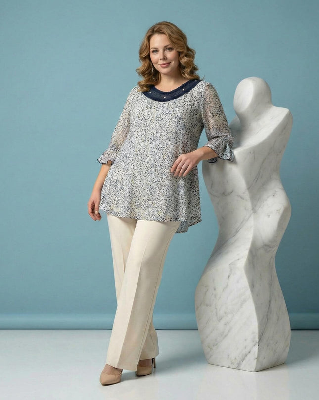 Επίσημη λευκή φλοράλ τουνίκ με πέρλες και τούλι σε μεγάλα μεγέθη, φωτογραφημένη σε ολόσωμη λήψη. Διαθέτει μανίκια 7/8 με βολάν και εντυπωσιακό ντεκολτέ.