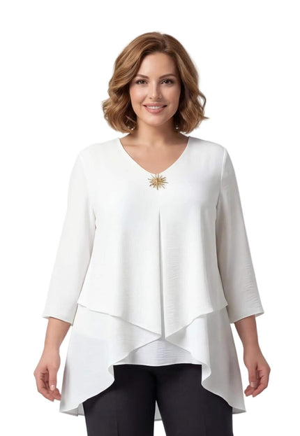 Λευκή επίσημη τουνίκ μεγάλα μεγέθη, εβαζέ και ασύμμετρη με χρυσή καρφίτσα στο λαιμόκοψη. Φωτογραφία μέχρι τη μέση, σε λευκό φόντο.