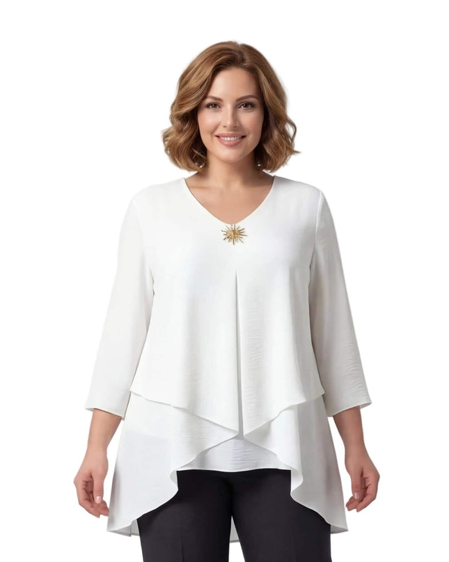 Λευκή επίσημη τουνίκ μεγάλα μεγέθη, εβαζέ και ασύμμετρη με χρυσή καρφίτσα στο λαιμόκοψη. Φωτογραφία μέχρι τη μέση, σε λευκό φόντο.