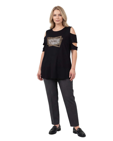 Ολόσωμη λήψη που δείχνει την επίσημη μαύρη τουνίκ plus size με ανοιχτούς ώμους και σχέδιο με στρας στο στήθος, φορεμένη με σκούρο παντελόνι.