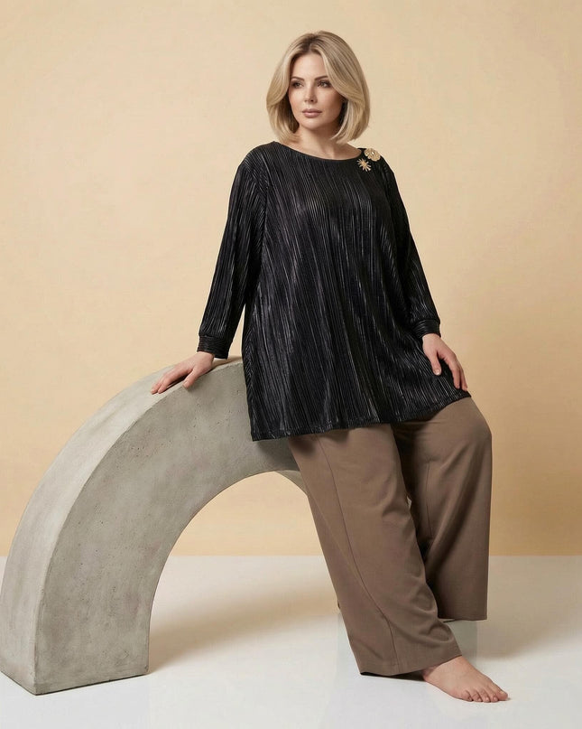 Ολόσωμη λήψη μοντέλου που φοράει επίσημη μαύρη τουνίκ σε μεγάλα μεγέθη. Διακρίνεται το πλισέ ύφασμα και η χρυσή καρφίτσα.