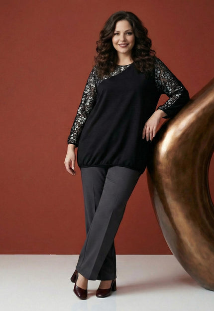 Επίσημη μαύρη τουνίκ plus size με φλοράλ δαντέλα στα μανίκια και λάστιχο στο τελείωμα, φορεμένη με γκρι παντελόνι σε ολόσωμη λήψη.