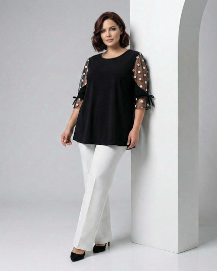 Ολόσωμη λήψη με επίσημη μαύρη τουνίκ plus size που διαθέτει εντυπωσιακά μανίκια από τούλι πουά και διακοσμητικούς φιόγκους, φορεμένη από μοντέλο.