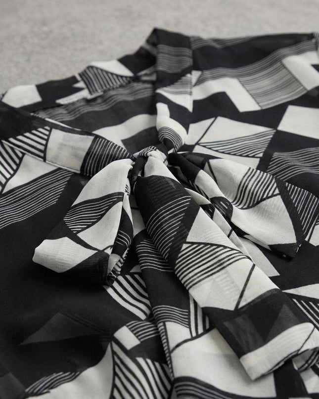 Κοντινή λεπτομέρεια που εστιάζει στο ντεκολτέ με τον δετό φιόγκο της τουνίκ σε μεγάλα μεγέθη, με ιδιαίτερο ασπρόμαυρο γεωμετρικό μοτίβο.