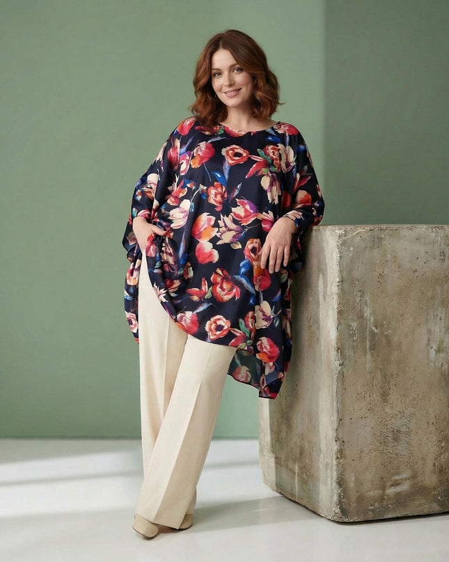 Ολόσωμη λήψη της επίσημης σκούρο μπλε φλοράλ τουνίκ πόντσο σε μεγάλα μεγέθη. Συνδυάζεται με ανοιχτόχρωμο παντελόνι, αναδεικνύοντας το ασύμμετρο τελείωμα.