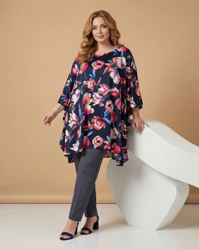 Ολόσωμη λήψη, σκούρο μπλε φλοράλ τουνίκ πόντσο σε μεγάλα μεγέθη, με αέρινα μανίκια και ασύμμετρο τελείωμα, συνδυασμένη με γκρι παντελόνι.