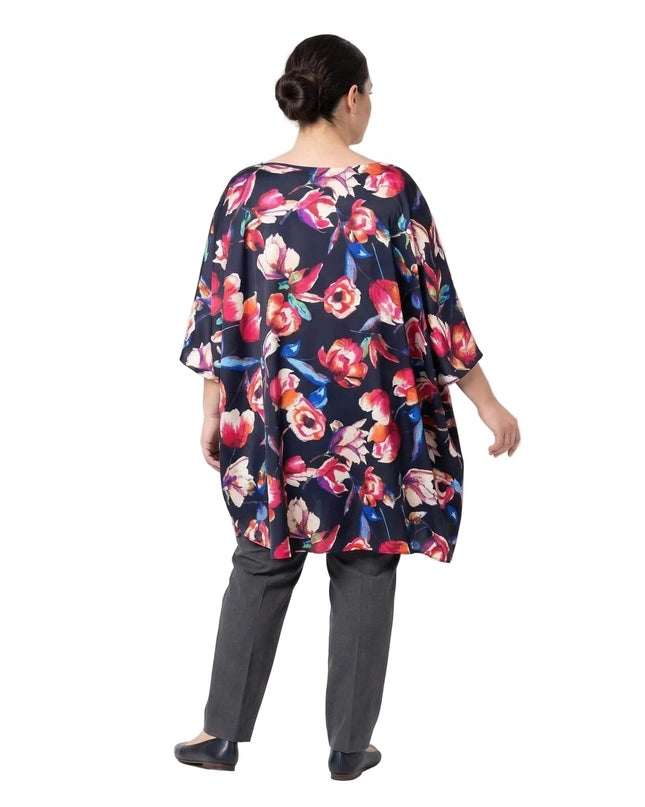 Πίσω όψη της κομψής σκούρο μπλε φλοράλ μάξι τουνίκ τύπου πόντσο σε μεγάλα μεγέθη, που αναδεικνύει την αέρινη εφαρμογή με τα φαρδιά μανίκια.