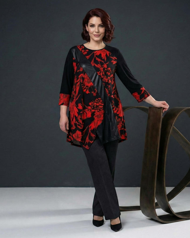 Επίσημη τουνίκ σε μεγάλα μεγέθη με κόκκινα λουλούδια και διαγώνια λεπτομέρεια δερματίνης, φορεμένη από μοντέλο σε ολόσωμη λήψη δίπλα σε διακοσμητικό.