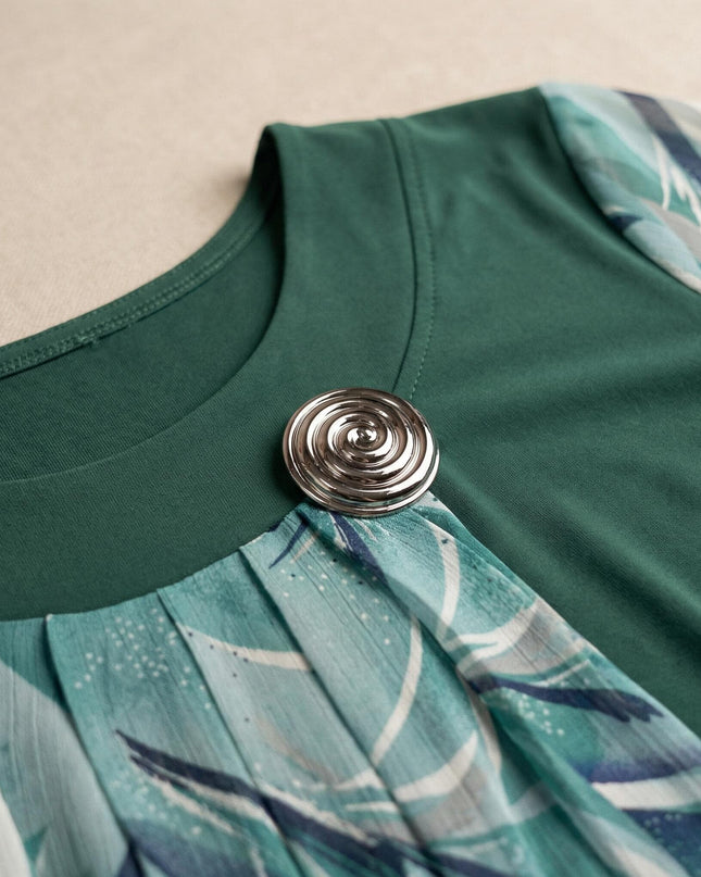 Κοντινή λεπτομέρεια από το ντεκολτέ επίσημης τουνίκ μεγάλα μεγέθη σε λαδί χρώμα, που εστιάζει στην ασημένια καρφίτσα και τις πτυχώσεις του φλοράλ σιφόν υφάσματος.