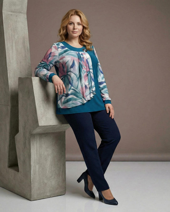 Ολόσωμη λήψη γυναίκας με επίσημη τουνίκ πετρόλ για μεγάλα μεγέθη, διακοσμημένη με σιφόν σε εμπριμέ σχέδιο φύλλων και καρφίτσα στο ντεκολτέ.