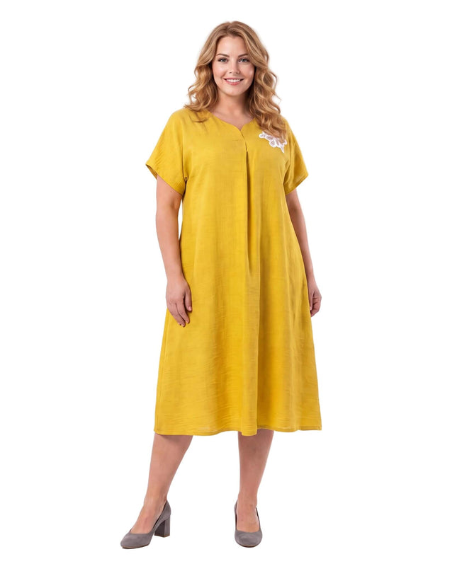 Κίτρινο plus size εβαζέ φόρεμα με V λαιμόκοψη, μπροστινή πιέτα και λευκή φλοράλ απλικέ λεπτομέρεια στον ώμο, σε λευκό φόντο.