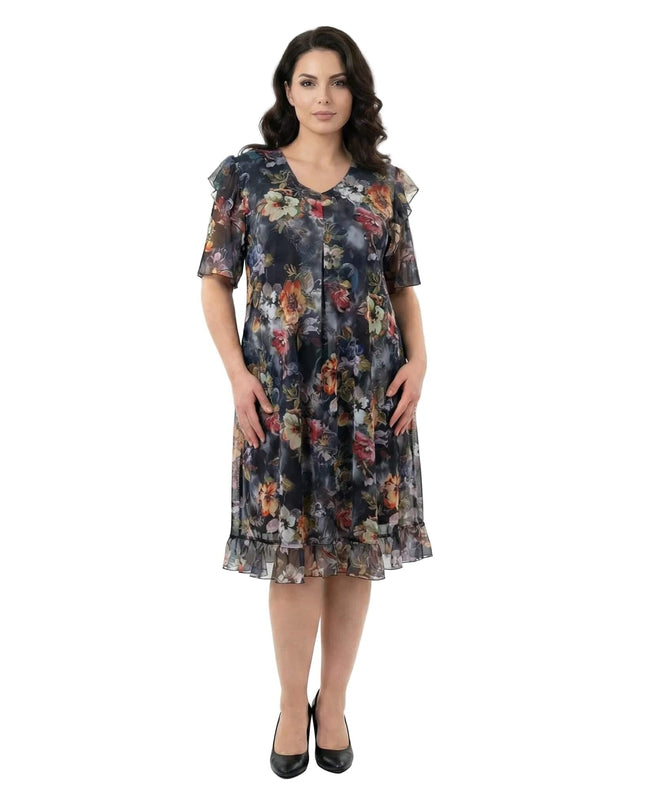 Επίσημο φλοράλ φόρεμα σιφόν σε μεγάλα μεγέθη με V λαιμόκοψη και βολάν στο τελείωμα, σε ολόσωμη φωτογραφία μπροστά σε λευκό φόντο.