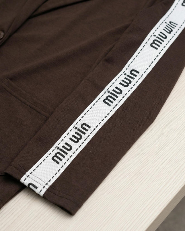 Κοντινή λεπτομέρεια από επίσημο γυναικείο σετ plus size σε καφέ χρώμα, εστιάζοντας στη λευκή διακοσμητική ρίγα με τυπωμένα γράμματα στο ύφασμα.