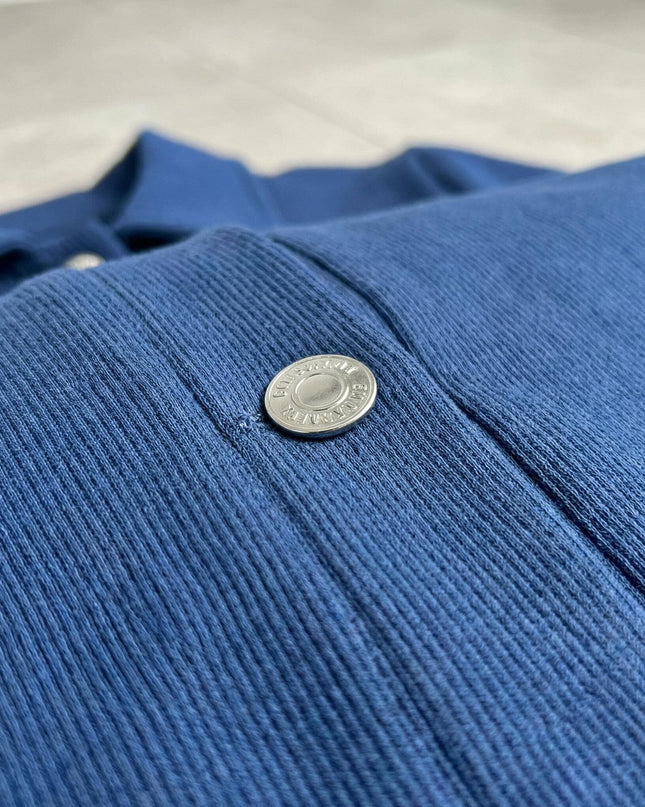 Κοντινή λεπτομέρεια από το μπλε γυναικείο σακάκι σε μεγάλα μεγέθη. Φαίνεται η ανάγλυφη υφή του υφάσματος και το ασημί μεταλλικό κουμπί.