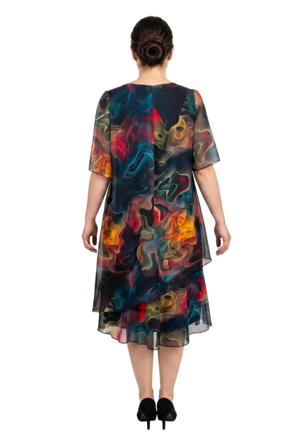 Πίσω όψη από επίσημο καλοκαιρινό φόρεμα plus size σε λευκό φόντο. Φτιαγμένο από ημιδιάφανο σιφόν με έντονο πολύχρωμο μοτίβο και ασύμμετρο τελείωμα.