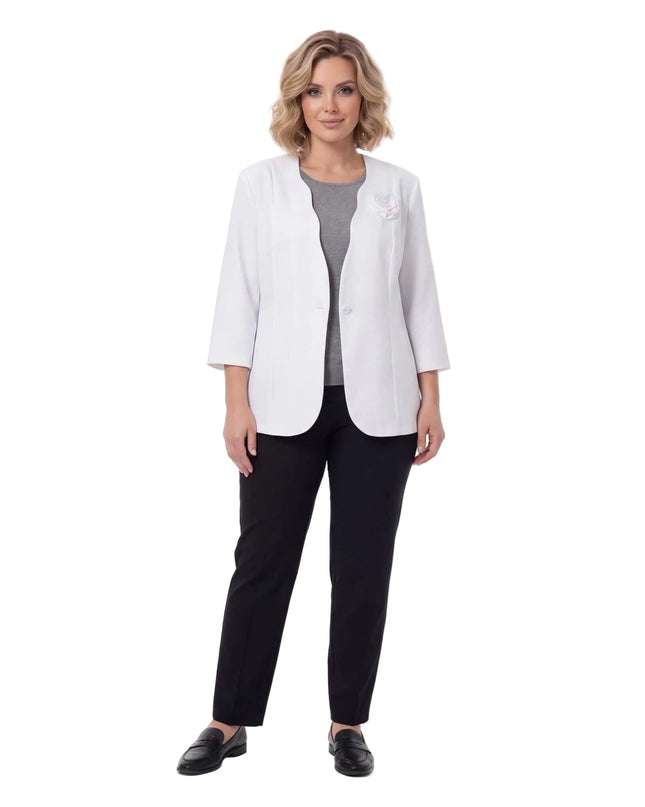 Ολόσωμη λήψη με γυναίκα να φοράει επίσημο λευκό σακάκι σε μεγάλα μεγέθη, συνδυασμένο με μαύρο παντελόνι και κομψή καρφίτσα τριαντάφυλλο.