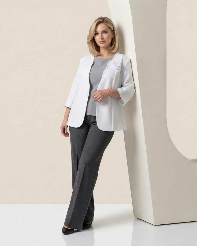 Ολόσωμη λήψη, επίσημο λευκό σακάκι σε μεγάλα μεγέθη με μανίκια 7/8 και κομψή καρφίτσα τριαντάφυλλο στο πέτο, συνδυασμένο με γκρι παντελόνι.