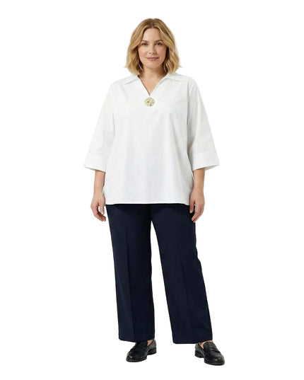 Ολόσωμη λήψη με γυναικείο επίσημο λευκό βαμβακερό πουκάμισο σε μεγάλα μεγέθη, διακοσμημένο με καρφίτσα στο ντεκολτέ και συνδυασμένο με σκούρο παντελόνι.