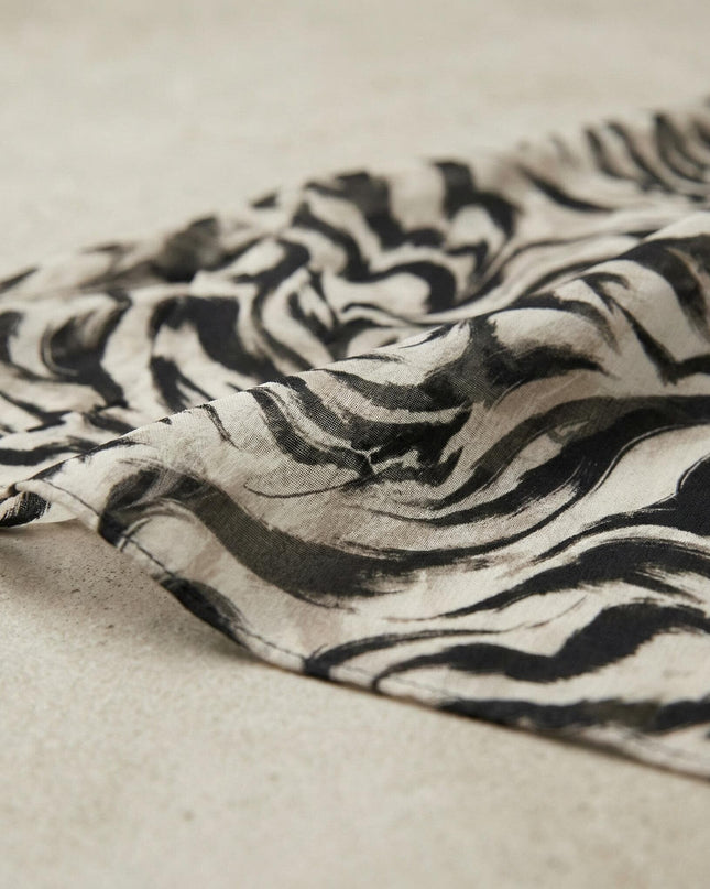 Κοντινή λεπτομέρεια της υφής του σιφόν υφάσματος από το επίσημο φόρεμα σε μεγάλα μεγέθη, με ιδιαίτερο αφηρημένο μοτίβο σε μαύρο και εκρού χρώμα.