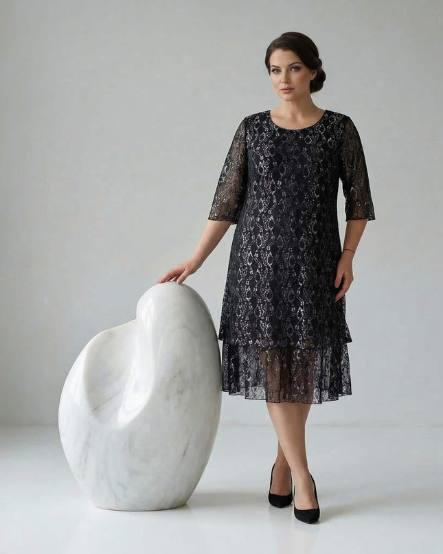 Ολόσωμη λήψη που δείχνει το επίσημο μαύρο φόρεμα σε μεγάλα μεγέθη με λουλουδάτη δαντέλα, διάφανα 3/4 μανίκια και κλιμακωτό τελείωμα σε λευκό φόντο.