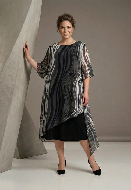 Επίσημο μαύρο φόρεμα plus size σε ολόσωμη λήψη, με ασύμμετρη μουσελίνα και ντεγκραντέ μοτίβο σε μαύρους και γκρι τόνους.