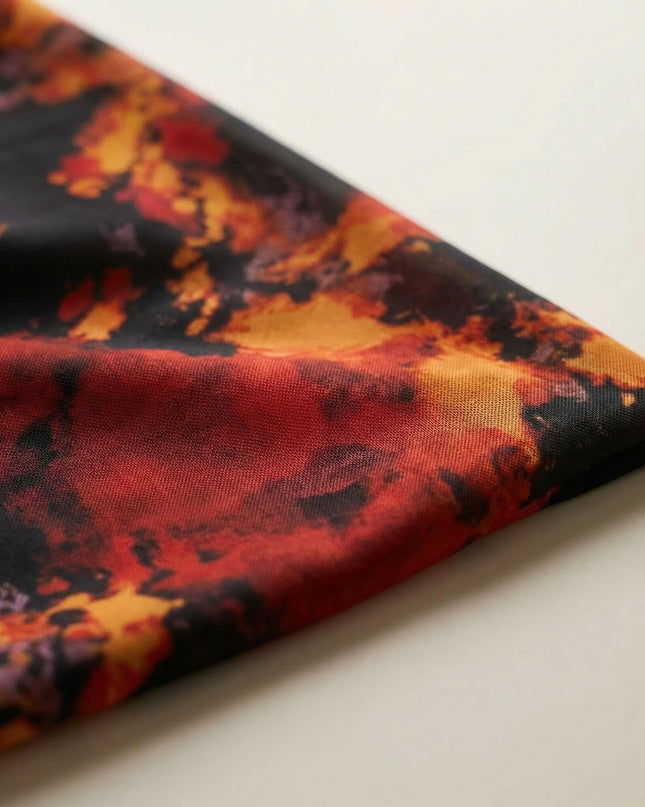 Κοντινή λεπτομέρεια υφάσματος από επίσημο μάξι φόρεμα για μεγάλα μεγέθη. Διακρίνεται το εντυπωσιακό φλογερό εμπριμέ σε αποχρώσεις κόκκινου και πορτοκαλί.