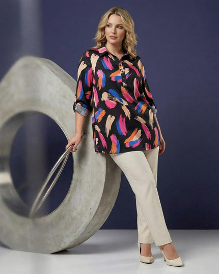 Ολόσωμη λήψη: Επίσημο μάξι πουκάμισο plus size με πολύχρωμο αφηρημένο μοτίβο και φαρδιά μανίκια, φορεμένο από μοντέλο με ανοιχτόχρωμο παντελόνι.