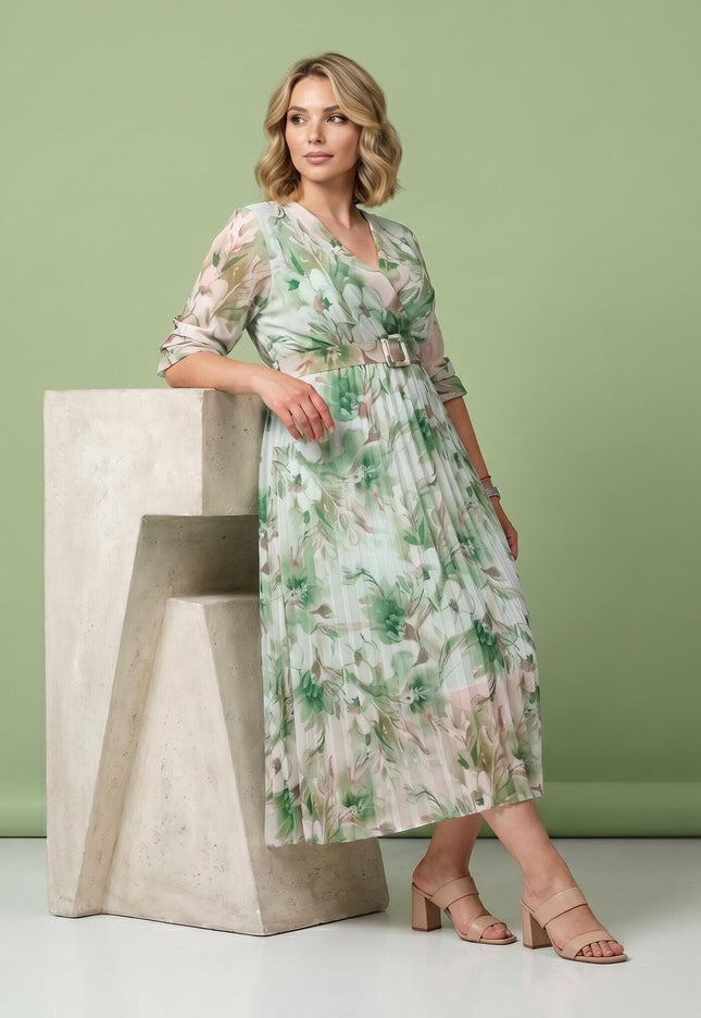 Ολόσωμη λήψη: Επίσημο μίντι φόρεμα plus size με πράσινο φλοράλ μοτίβο, κρουαζέ V-ντεκολτέ, ζώνη και πλισέ φούστα.