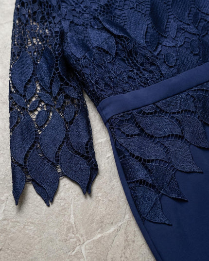 Κοντινή λεπτομέρεια που εστιάζει στο μανίκι με δαντέλα του επίσημου μπλε σκούρου φορέματος σε μεγάλα μεγέθη, αναδεικνύοντας το φλοράλ σχέδιο και την υφή του υφάσματος.