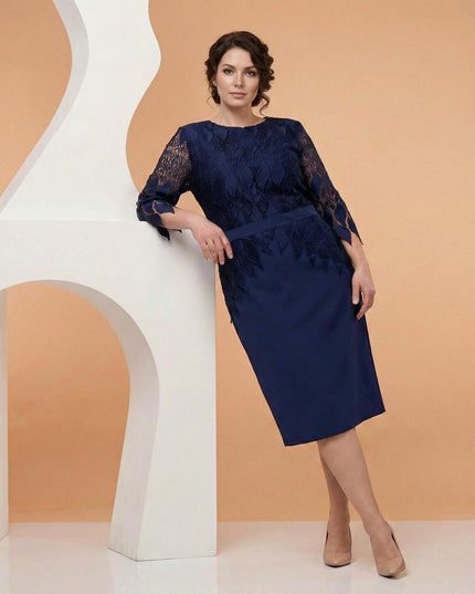 Επίσημο μπλε σκούρο φόρεμα σε μεγάλα μεγέθη με δαντέλα και μανίκια 7/8, σε ολόσωμη λήψη με το μοντέλο να ακουμπά σε λευκό διακοσμητικό.