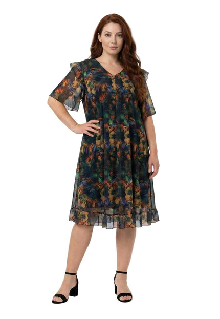 Επίσημο plus size φόρεμα από χρωματιστό σιφόν με φλοράλ μοτίβο και βολάν στο τελείωμα, σε ολόσωμη λήψη που αναδεικνύει την άνετη εβαζέ γραμμή.