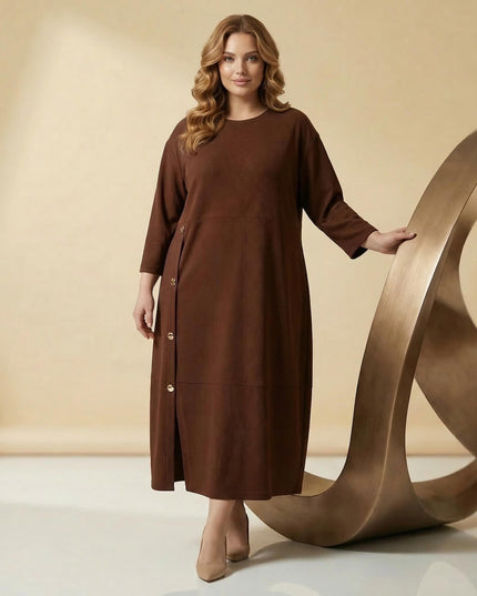 Ολόσωμη λήψη μοντέλου με επίσημο καφέ μάξι φόρεμα plus size. Ξεχωρίζει η ασύμμετρη σειρά με διακοσμητικά χρυσά κουμπιά και η άνετη εβαζέ γραμμή.