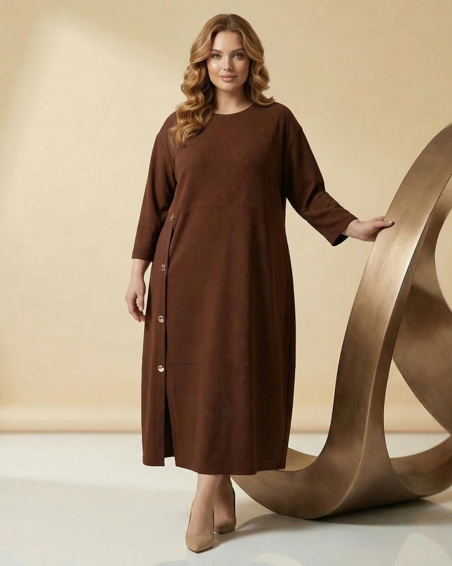 Ολόσωμη λήψη μοντέλου με επίσημο καφέ μάξι φόρεμα plus size. Ξεχωρίζει η ασύμμετρη σειρά με διακοσμητικά χρυσά κουμπιά και η άνετη εβαζέ γραμμή.