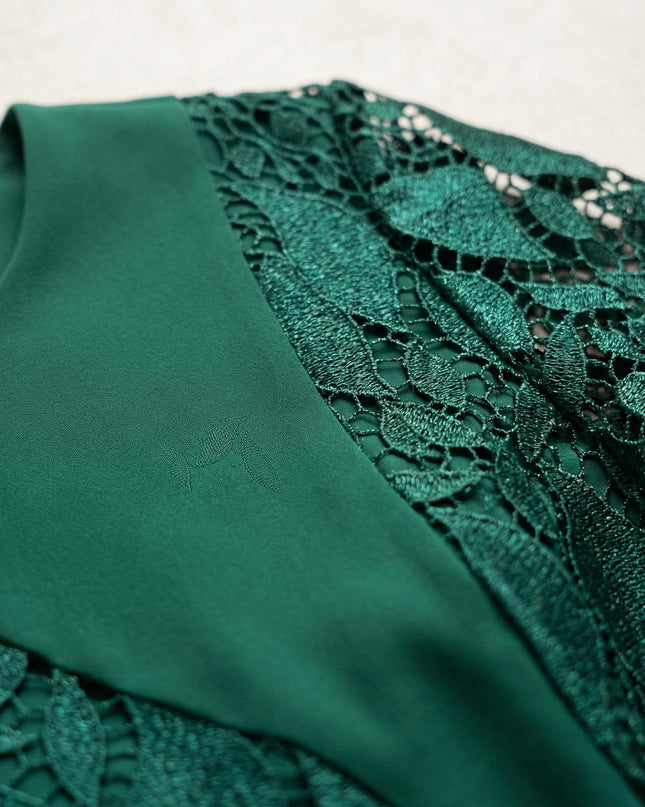 Κοντινή λεπτομέρεια από επίσημο πράσινο φόρεμα σε μεγάλα μεγέθη, εστιάζοντας στην ανάγλυφη υφή της δαντέλας με μοτίβα φύλλων και την ποιότητα του υφάσματος.